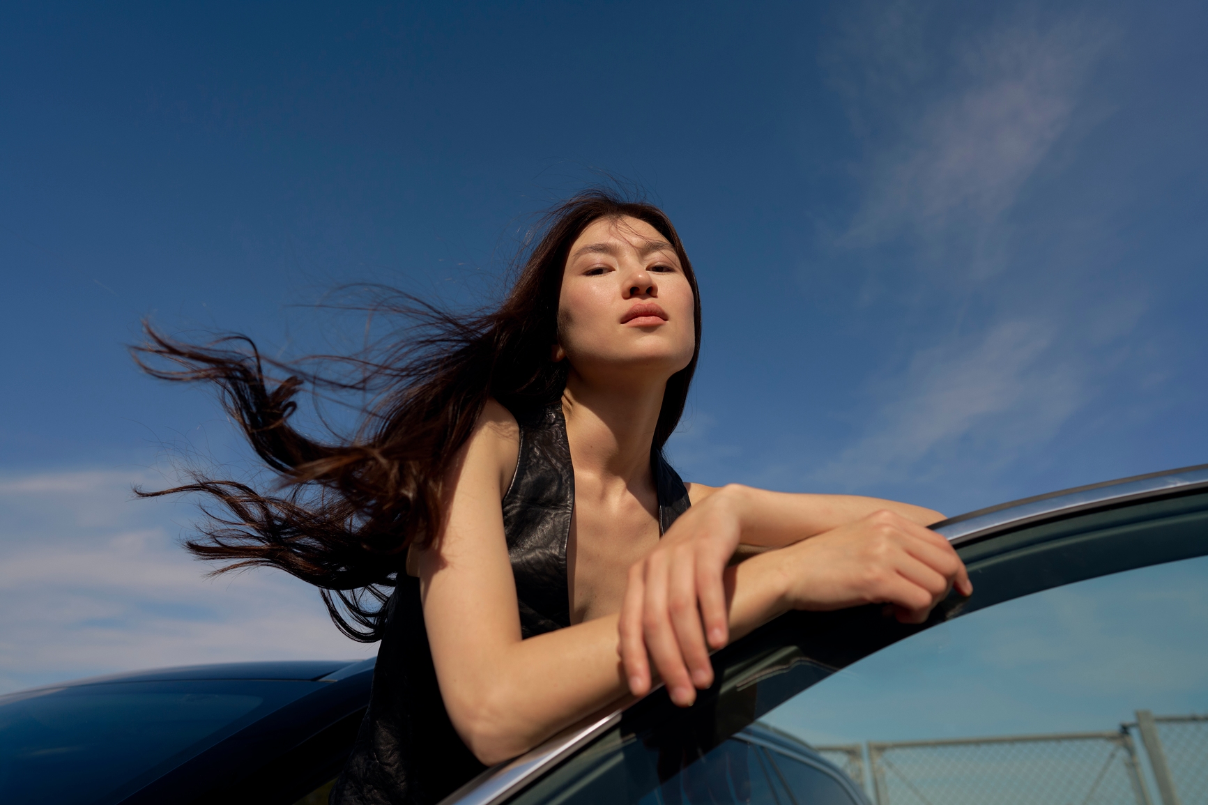 Woman leaning on a car under a blue sky